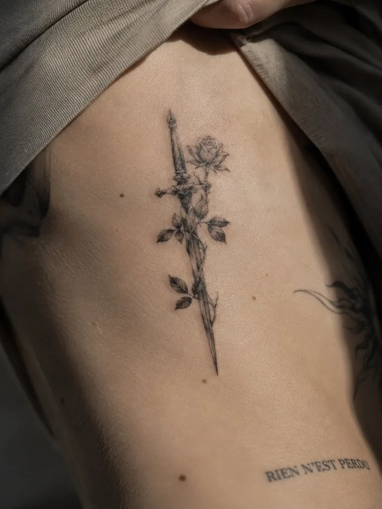 A fine-line rose with a long stem tattooed down the ribs